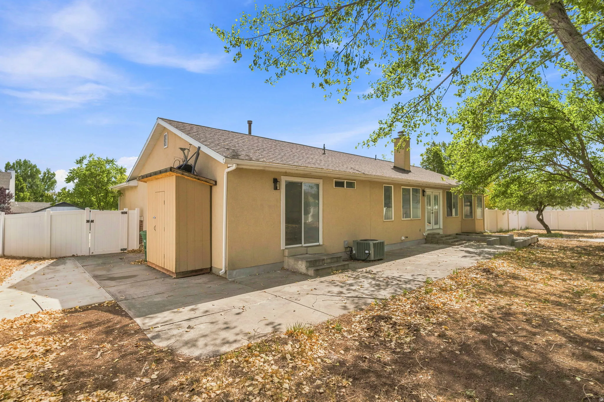 Rear exterior featuring stucco siding, a concrete patio, and mature trees
