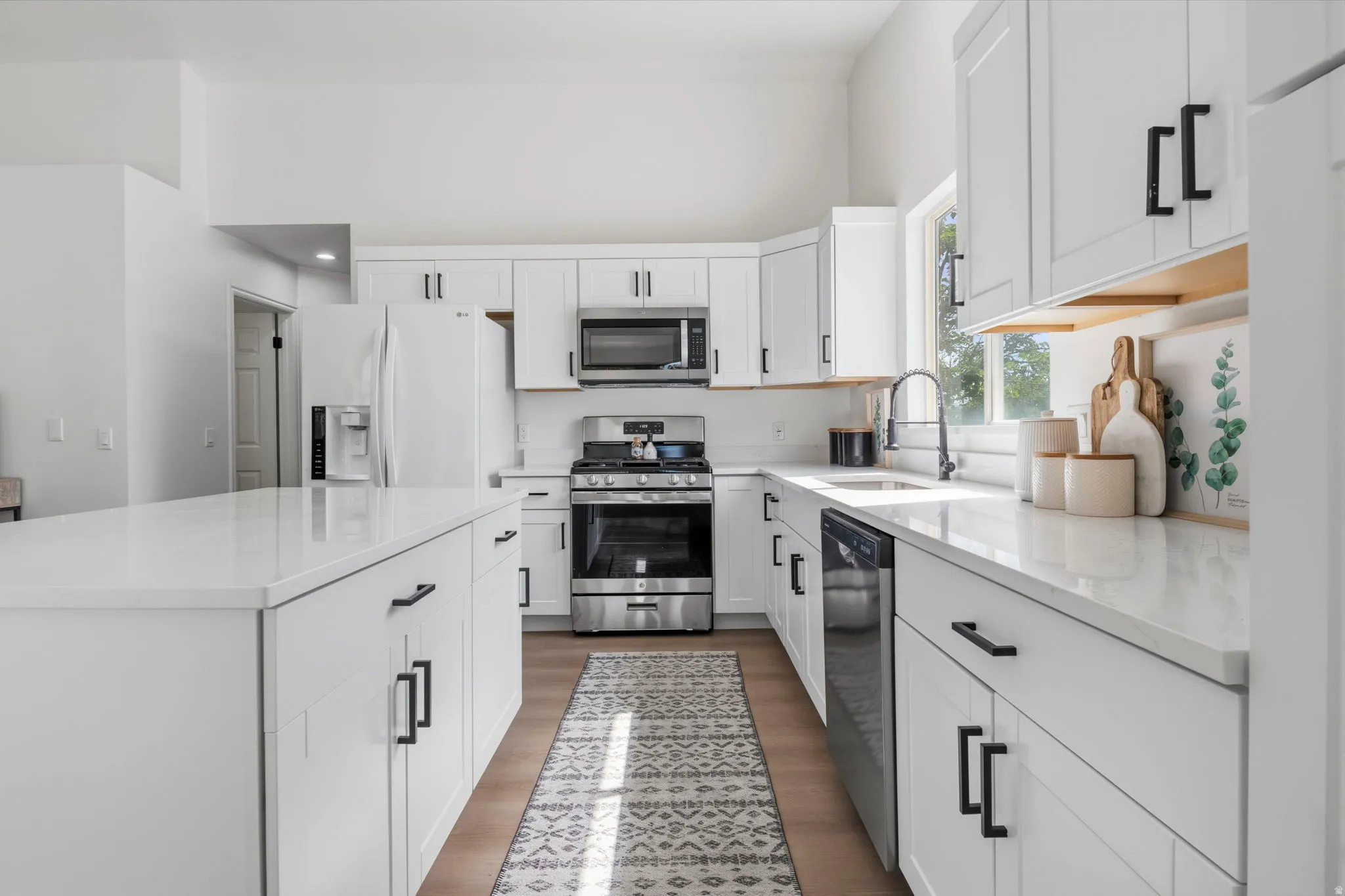 Bright kitchen featuring white cabinetry with black hardware, white countertops, wood-finish flooring, and stainless steel appliances