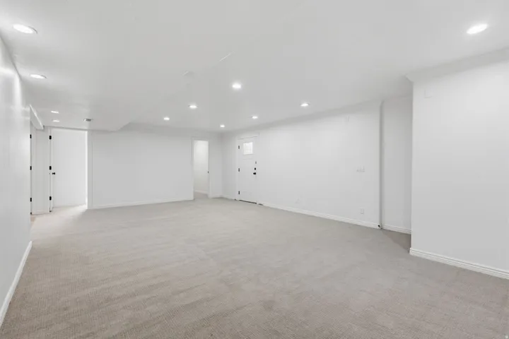 Spacious room with recessed lighting, light-toned carpeting, white walls, and multiple doorways