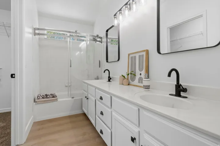 Bathroom featuring a dual vanity with white cabinetry, matte black hardware, and stone-finish countertops