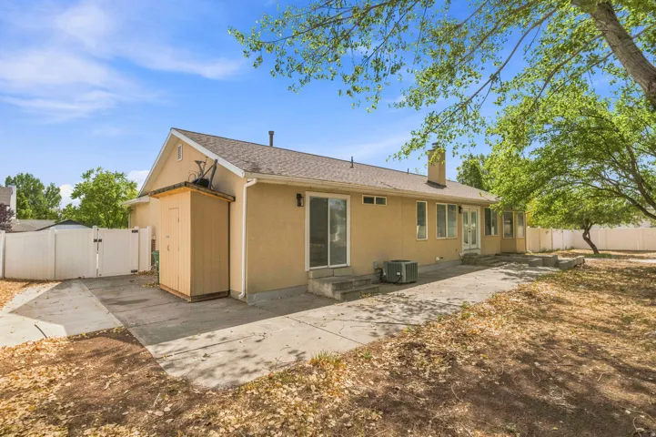Rear exterior featuring stucco siding, a concrete patio, and mature trees