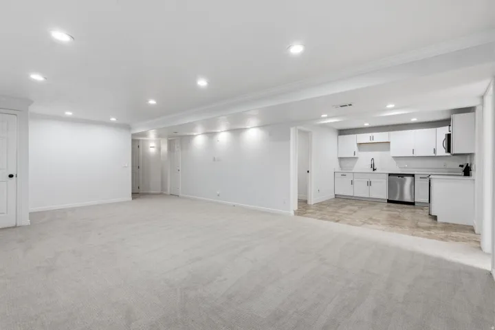 Expansive carpeted area complemented by a full kitchen featuring white cabinetry, stainless steel appliances, and tile flooring