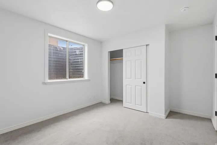 Neutral wall color, carpeted flooring, window with white trim, built-in closet with sliding doors, and ceiling-mounted light fixture
