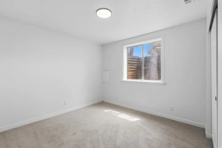 Neutral wall color, carpet flooring, window with white trim, and a flush-mount ceiling light