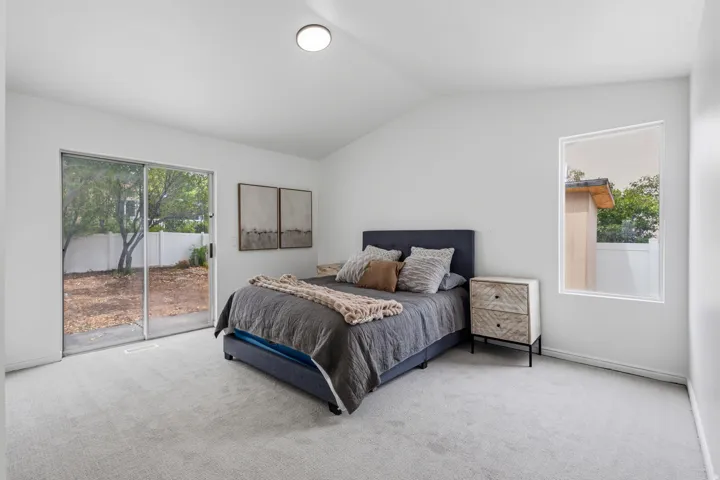 Vaulted ceiling, recessed lighting, expansive sliding glass door, single fixed window, and light-toned carpeting