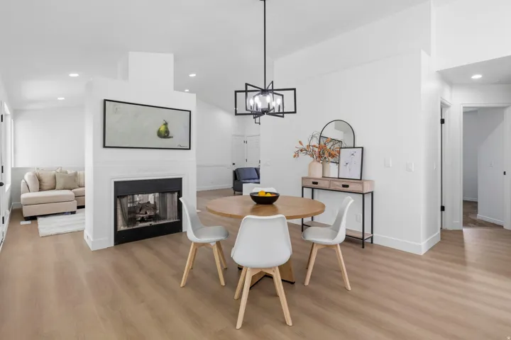 Open-concept living space with a central fireplace, light wood-finish flooring, recessed lighting, and a modern geometric chandelier
