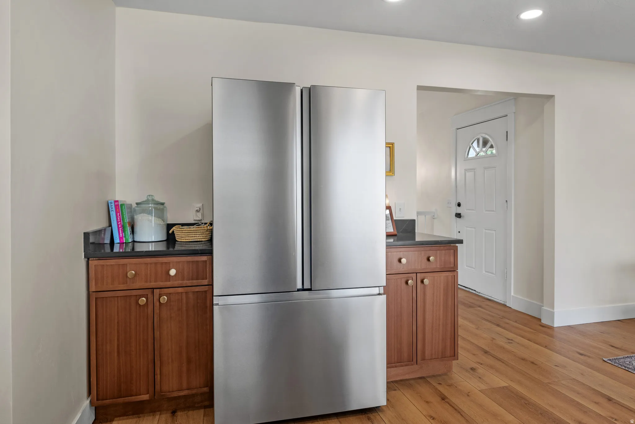 Stainless steel French door refrigerator flanked by dark wood cabinetry with gold-toned hardware