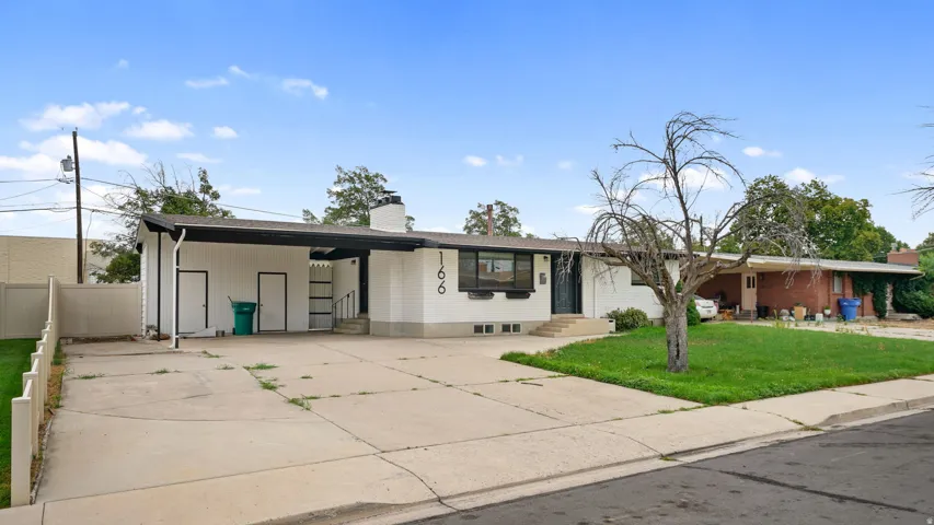 Mid-century modern residence featuring a concrete driveway, carport, and a white facade with black trim
