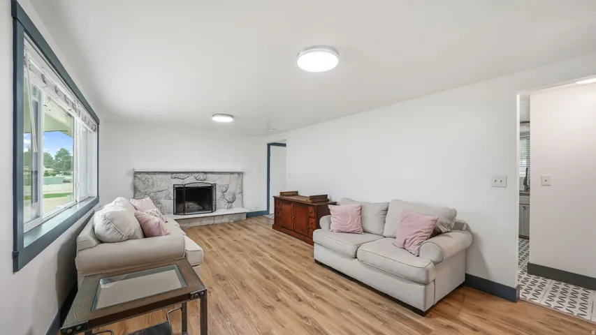 Spacious living area featuring wood-finish flooring, a stone fireplace, large windows with dark trim, recessed lighting, and white walls