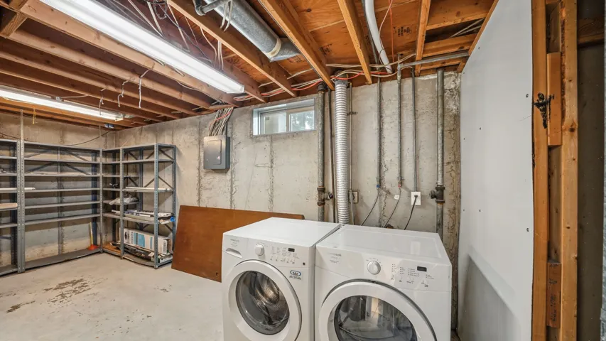 Basement area featuring concrete walls and flooring, exposed wood ceiling joists, and fluorescent lighting