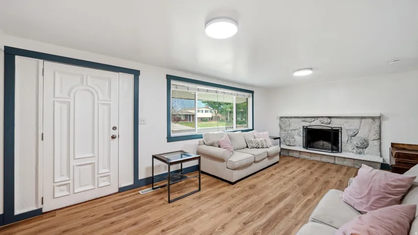 Living area featuring wood-finish flooring, a stone fireplace with a black firebox, and a front entry door with decorative panels and sidelights