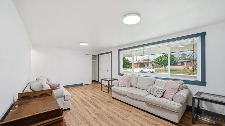 Bright living area featuring wood-finish flooring, white walls, and a wide picture window with dark trim