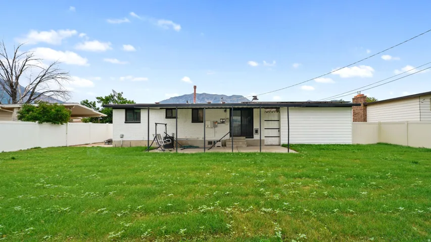 Expansive backyard featuring a lush lawn, white privacy fencing, and a concrete patio