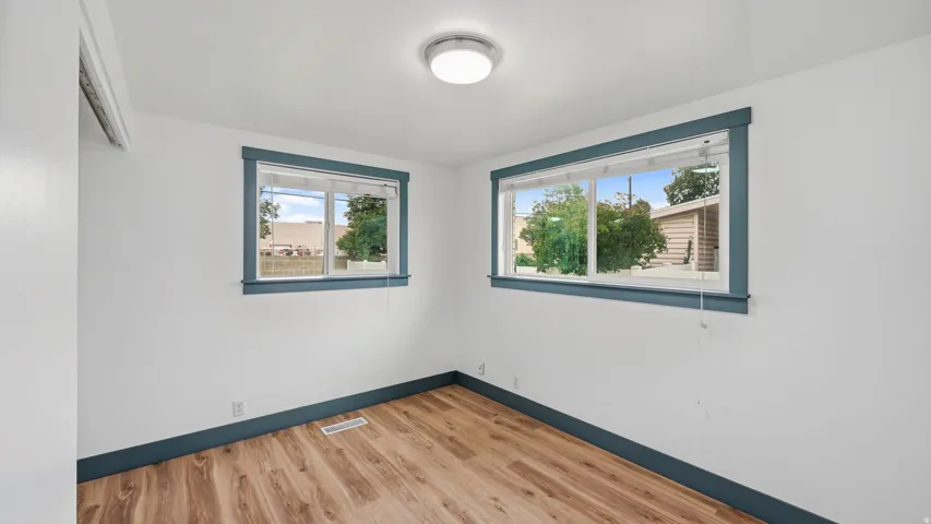 Room with wood-finish flooring, two windows with blinds, and a flush-mount ceiling light