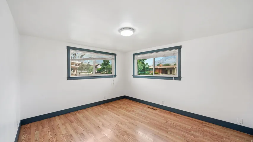Room featuring wood-finish flooring, two large windows with dark trim, white wall finishes, and a flush-mount ceiling light fixture