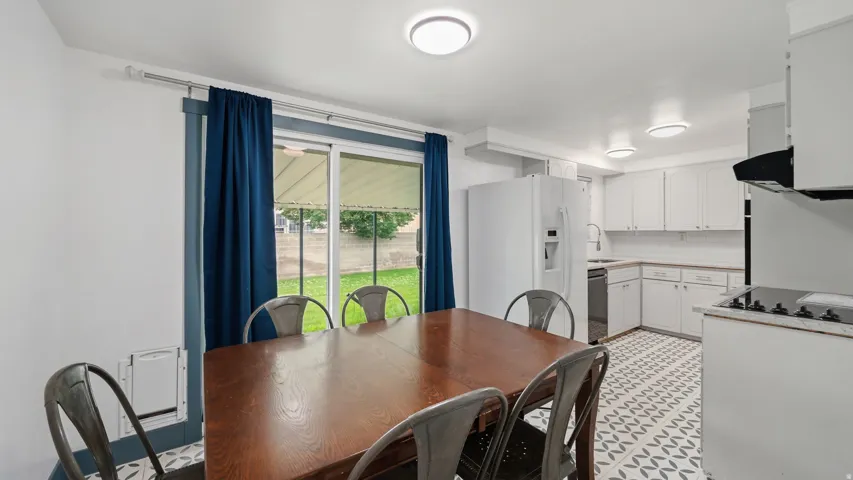 Open-concept kitchen and dining area featuring white cabinetry, a built-in range with an overhead vent hood, a stainless steel dishwasher, and patterned tile flooring