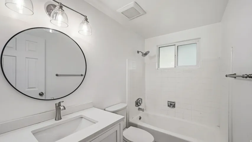 Contemporary bathroom featuring a white vanity with an integrated sink, a circular mirror with a black frame, and a three-light vanity fixture