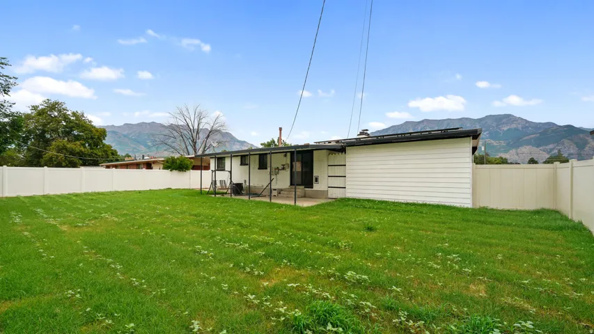 Expansive rear yard featuring green lawn, privacy fencing, and a covered concrete patio