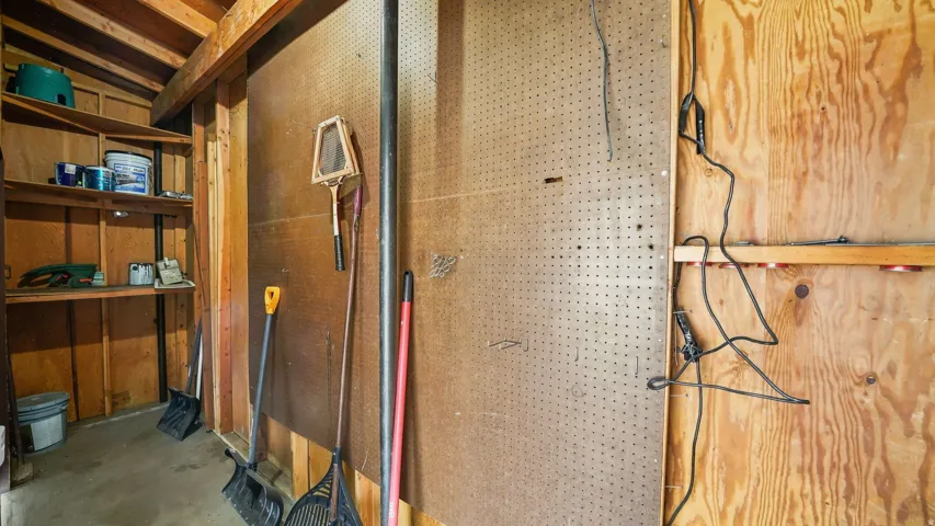 Utility storage area featuring exposed wood framing, built-in shelving, and pegboard organization