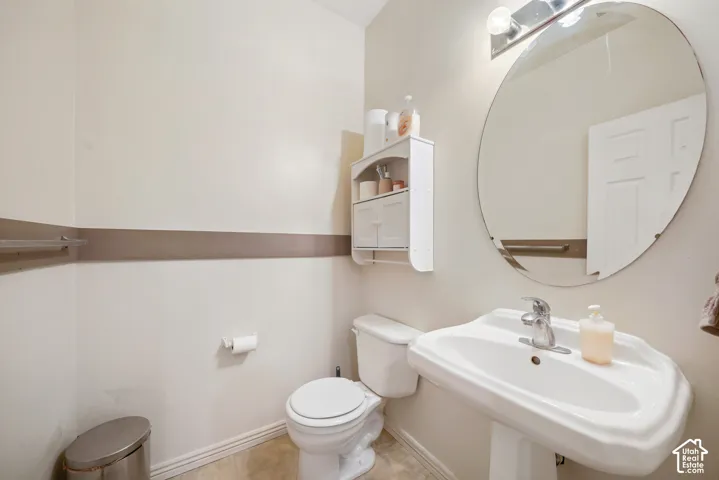 Pedestal sink with chrome faucet, circular mirror, and wall-mounted light fixture