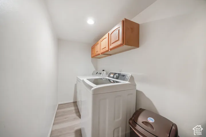 Dedicated laundry area featuring wood-finish cabinetry, recessed lighting, and light wood-look flooring