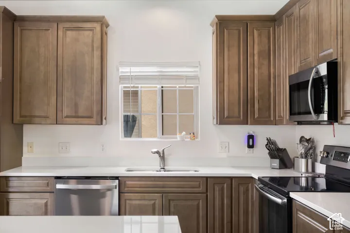 Kitchen featuring wood-finish cabinetry, white countertops, a stainless steel sink with a modern faucet, an over-range microwave, and a window with blinds
