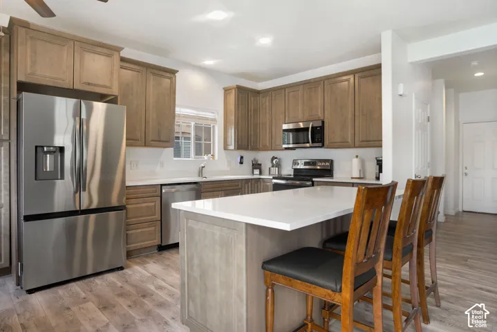 Modern kitchen featuring stainless steel appliances, light wood-finish cabinetry, white countertops, and wood-finish flooring