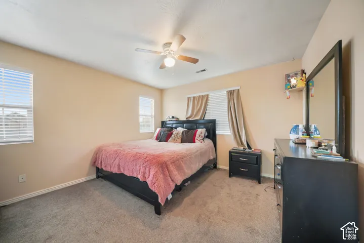 Carpeted room featuring a ceiling fan with integrated lighting, multiple windows with blinds, and neutral-toned walls