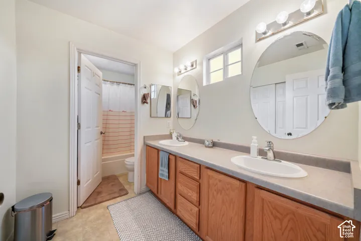 Dual vanity featuring wood-finish cabinetry, integrated sinks, and individual circular mirrors