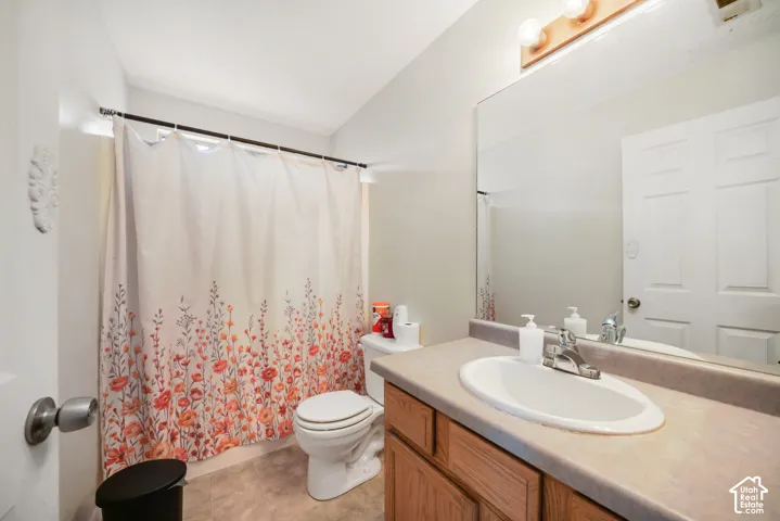 Bathroom featuring a wood-finish vanity with a built-in sink, a large wall-mounted mirror, overhead vanity lighting, and a white toilet