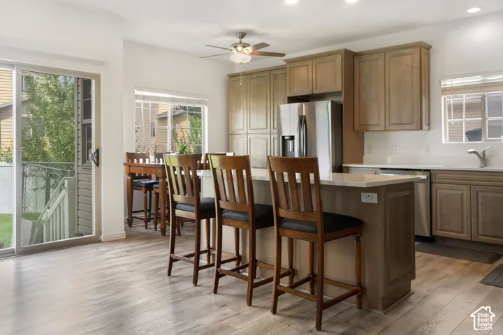 Kitchen featuring light wood-finish cabinetry, stainless steel appliances, a white countertop island with seating, and wood-finish flooring