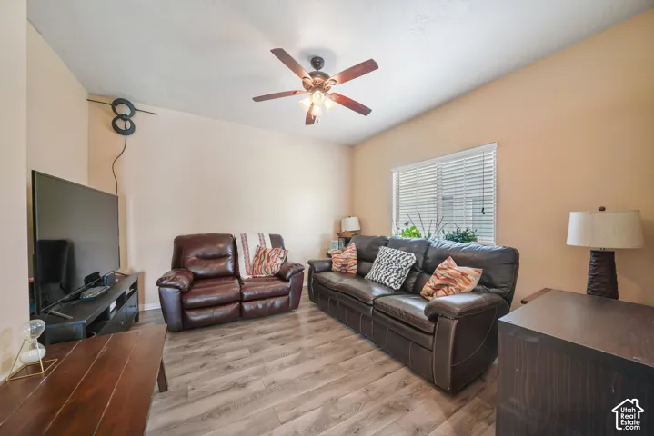 Living area featuring wood-finish flooring, a ceiling fan with integrated lighting, and a window with horizontal blinds