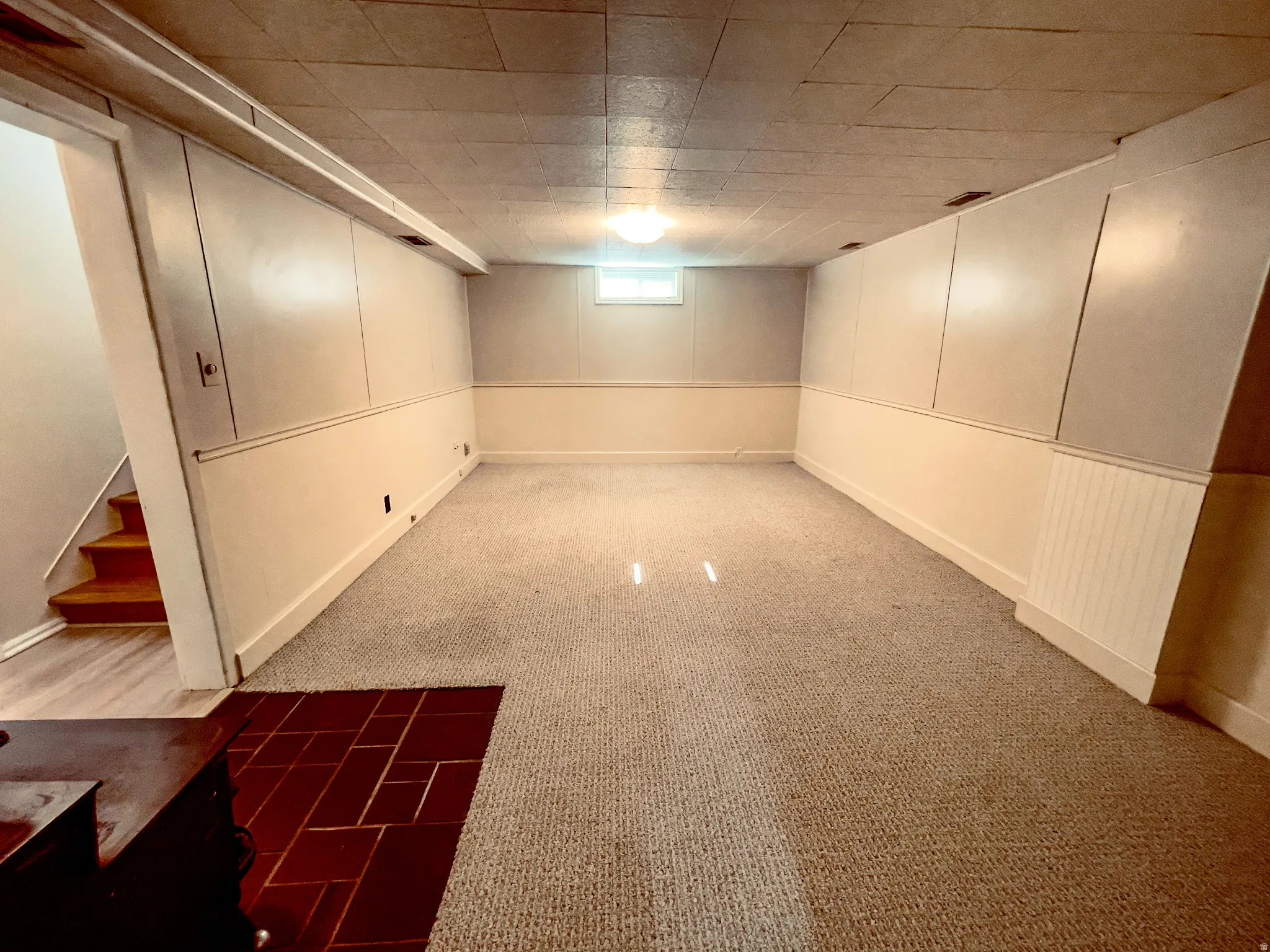 Finished basement space featuring light-toned carpeting and a small window for natural light