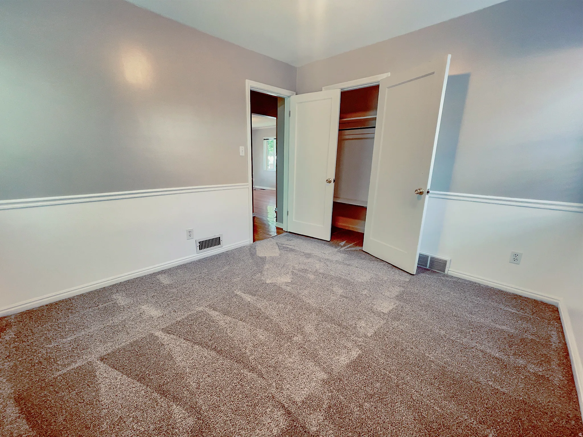 Neutral-toned carpeting paired with a two-tone wall treatment featuring chair rail molding