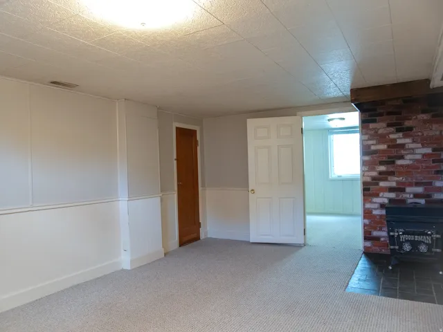 Brick accent wall with a black wood stove, carpeted flooring, and a white paneled ceiling