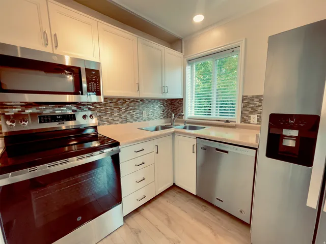 Kitchen featuring stainless steel appliances, light wood-finish flooring, white cabinetry, a mosaic tile backsplash, and a window with blinds