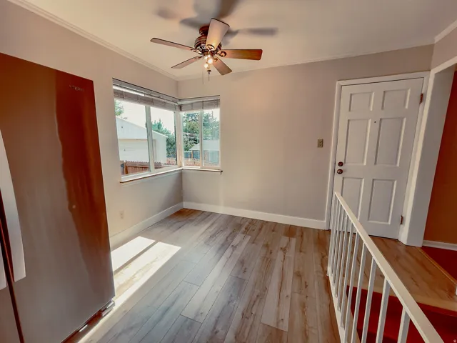 Corner window arrangement, wood-finish flooring, ceiling fan with light kit, crown molding, and a paneled door