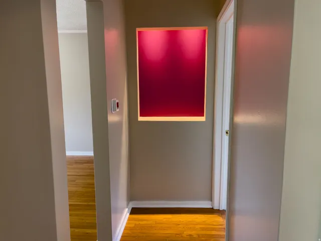 Hallway with recessed wall feature, rich wood-finish flooring, and crisp white baseboards