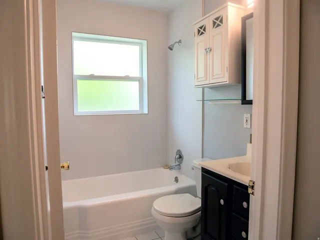 Bathroom featuring a white bathtub, a frosted window, a dark wood vanity with a white countertop, an overhead wall cabinet, and a mirrored medicine cabinet