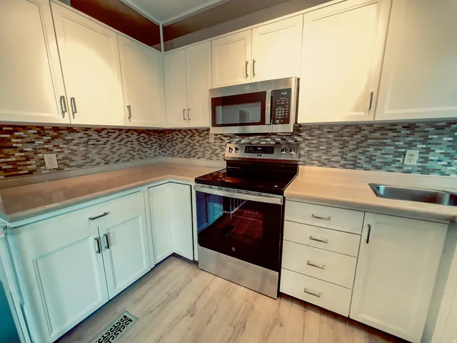 Kitchen featuring white cabinetry, light-toned countertops, a mosaic tile backsplash, stainless steel appliances, and wood-finish flooring