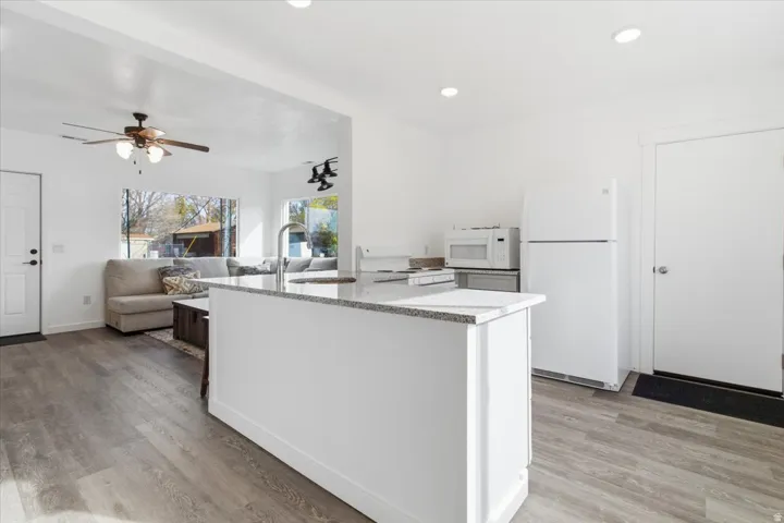 Open-concept kitchen featuring a white island with a granite-style countertop, recessed lighting, and wood-finish flooring