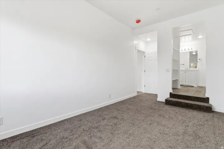 Carpeted room featuring white walls, a recessed lighting fixture, and a doorway opening to a bathroom with a white vanity, built-in shelving, and wood-finish flooring