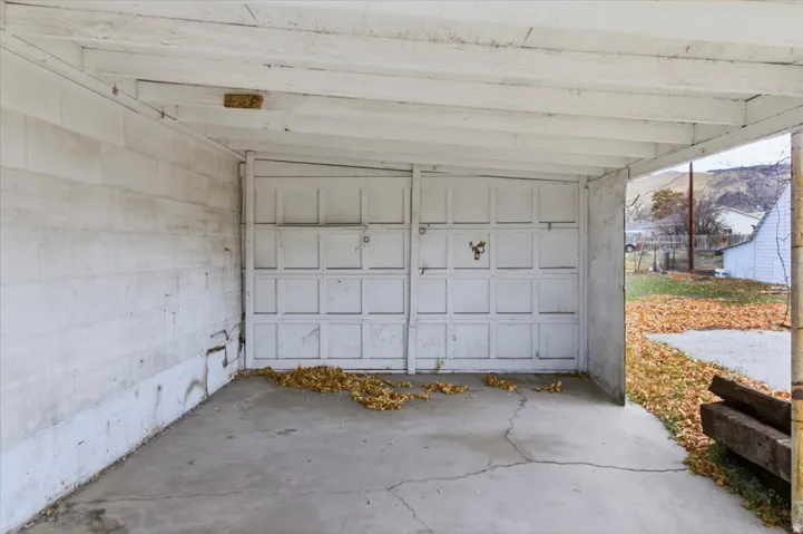 Carport structure featuring a painted wood-beam ceiling, concrete flooring, and an attached garage door