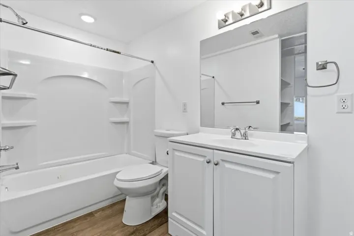 Bathroom featuring a white tub/shower combination with integrated shelving, a single vanity with storage, and wood-finish flooring