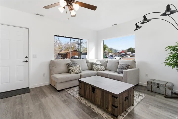 Bright living area featuring wood-finish flooring, white walls, large windows, and an overhead ceiling fan