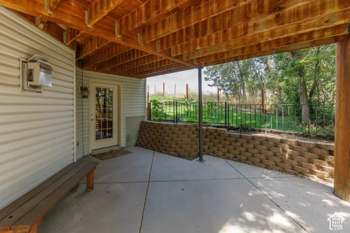 Covered concrete patio featuring exposed wood beam ceiling, white siding, and a glass-paneled door