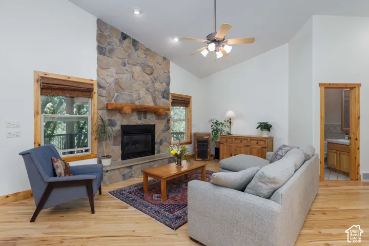 Spacious living area featuring a stone fireplace with a substantial wood mantle, vaulted ceiling, wood-finish flooring, and natural wood window frames