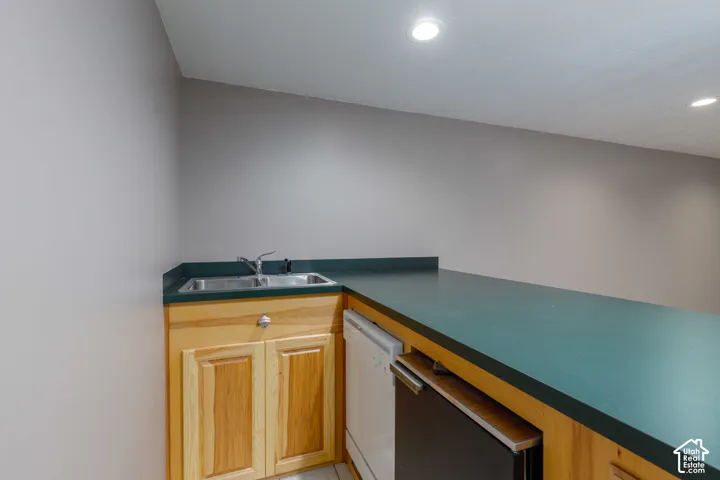 Kitchenette featuring a stainless steel double sink, wood cabinetry, built-in dishwasher, and a beverage refrigerator