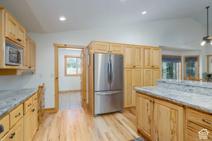 Kitchen featuring wood-finish cabinetry, stone countertops, stainless steel refrigerator, built-in microwave, and wood-finish flooring