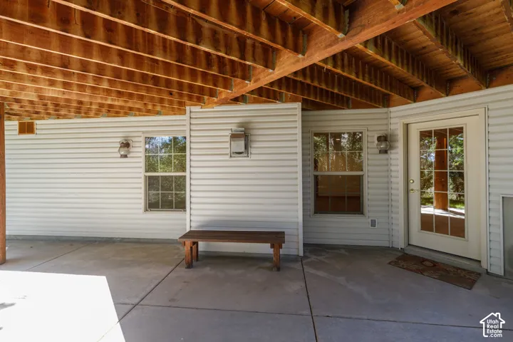 Covered concrete patio with exposed wood joists, white siding, and a glass-paneled entry door